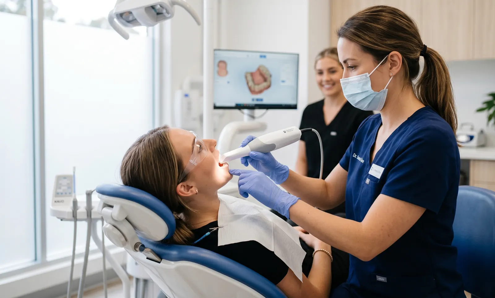 Dentist using an intraoral 3D scanner on a patient with a digital scan visible on the monitor